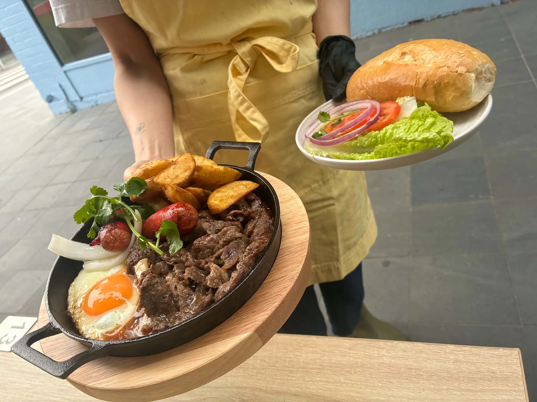 A Linnie Cafe team member serving sizzling steak with salad and bread